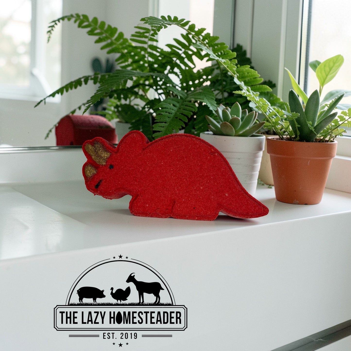 The Lazy Homesteader LLC Triceratops shaped red bath bomb with gold horns, perfect for kids' bath time fun.